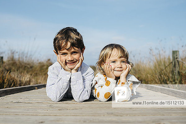 Porträt eines Jungen und seiner kleinen Schwester nebeneinander liegend auf der Promenade