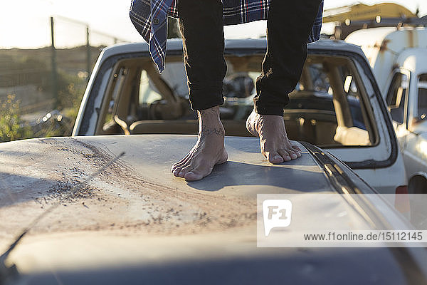 Young man walking barefoot on car roof on a scrapyard