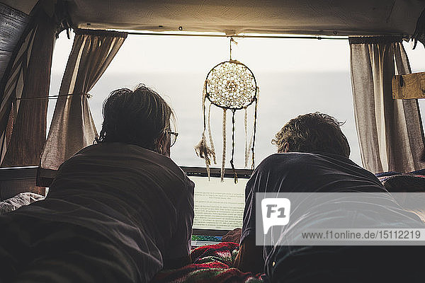 Älteres Ehepaar reist in einem Oldtimer-Lieferwagen  mit Laptop