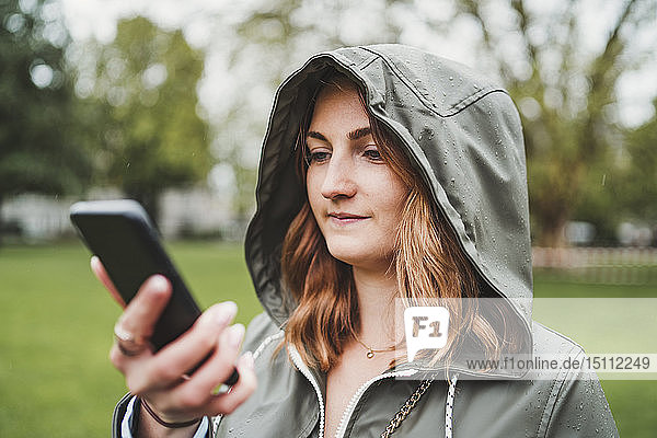 Young woman wearing hooded jacket and using cell phone on a rainy day