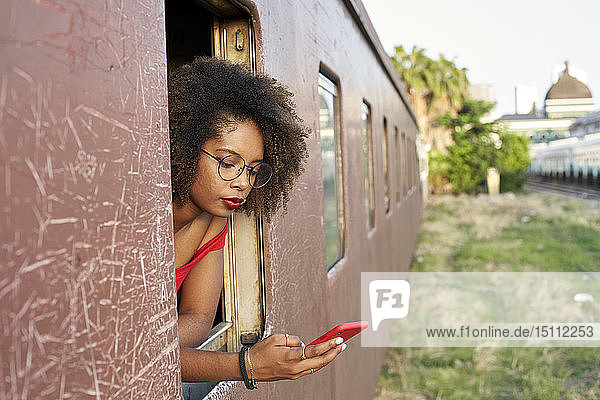 Junge Frau überprüft ihr Telefon am Fenster eines Zuges