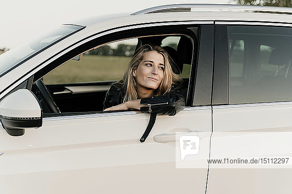 Blonde Frau in weißem Auto  die aus dem Fenster schaut