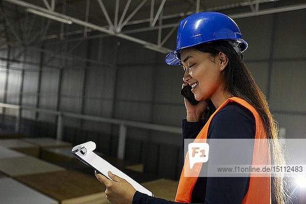 Lächelnde Arbeitnehmerin am Telefon im Fabriklager