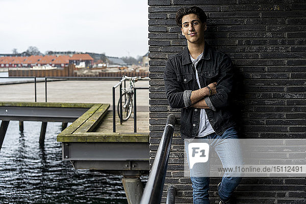 Dänemark  Kopenhagen  Porträt eines selbstbewussten jungen Mannes  der an einer Wand am Wasser lehnt