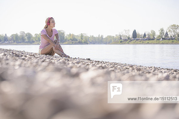 Reife Frau entspannt sich am Flussufer und hört Musik mit Kopfhörern