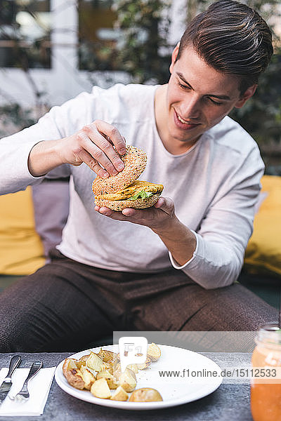 Young man sitting on couch in a restaurant having a vegan burger for lunch
