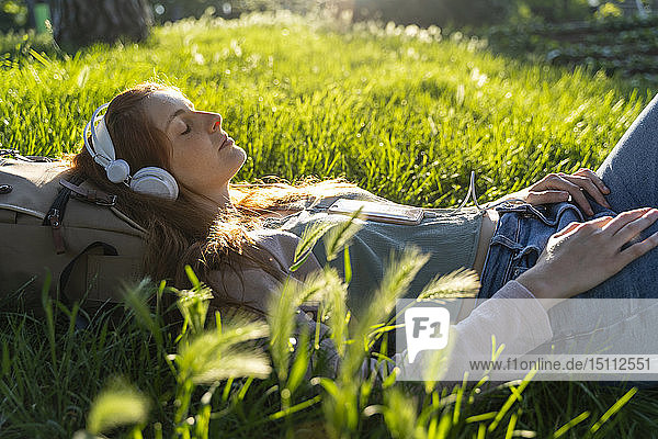 Junge rothaarige Frau mit Kopfhörern und Smartphone in einem Park
