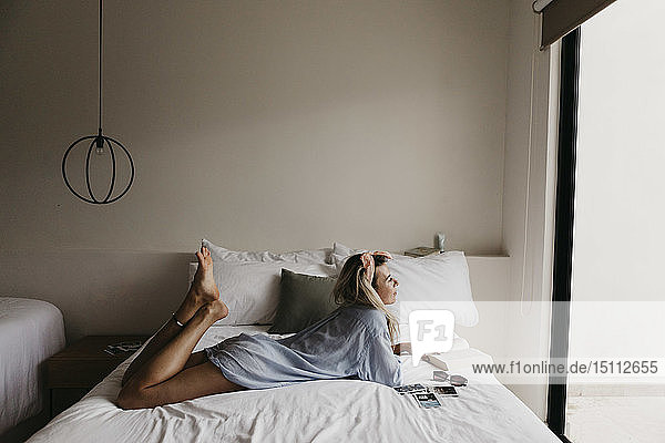 Junge Frau im Bett liegend mit Buch  Sonnenbrille und Polaroidbildern