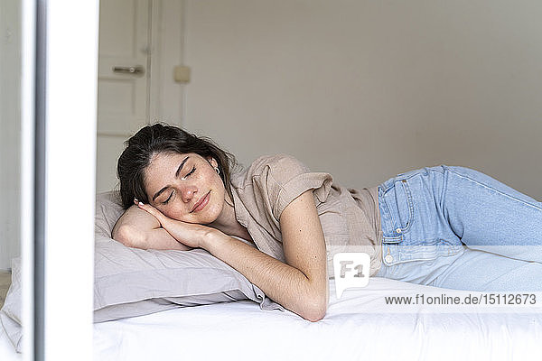 Smiling young woman lying on bed with closed eyes