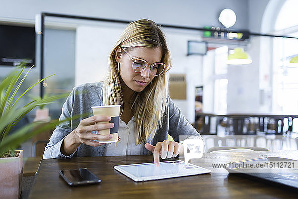 Junge Frau  die mit ihrem digitalen Tablet arbeitet  während sie im Café Kaffee trinkt