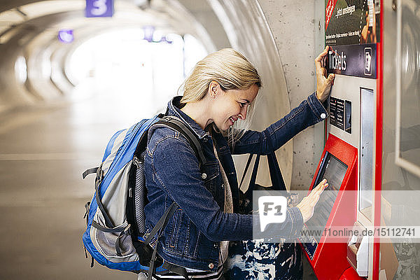 Smiling woman using ticket machine at the station