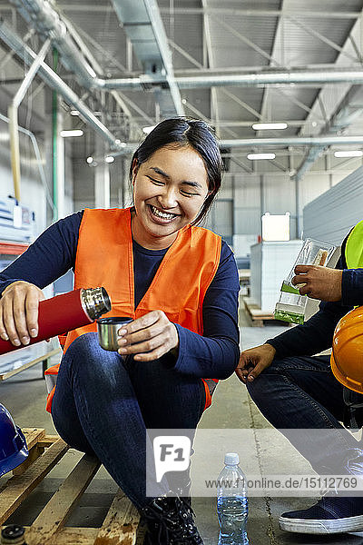 Happy female worker pouring drink into mug during lunch break in factory