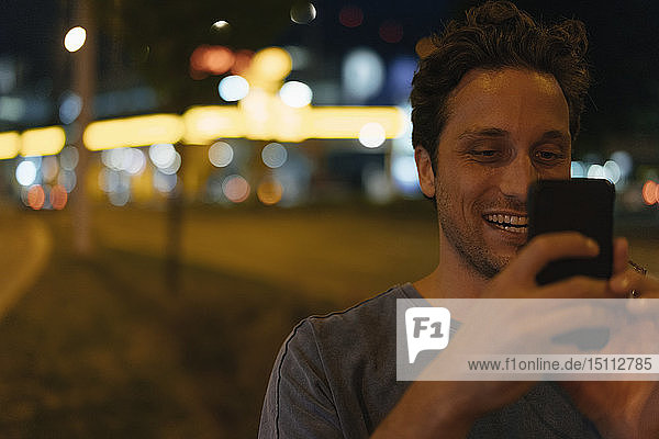 Happy young man using cell phone in the city at night