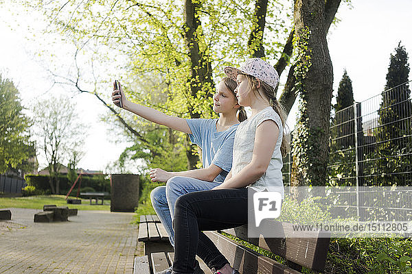 Two girls sitting on a park bench taking a selfie