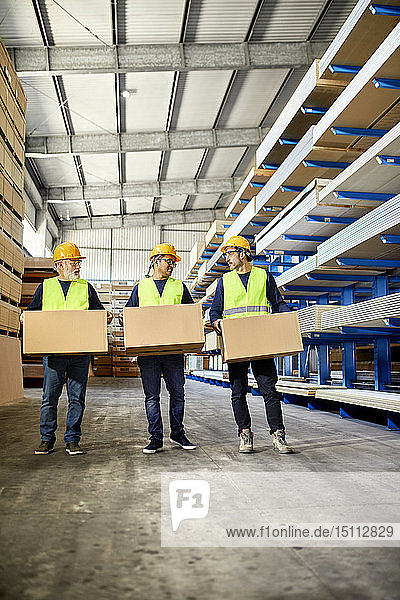 Drei Arbeiter tragen Kisten im Fabriklager