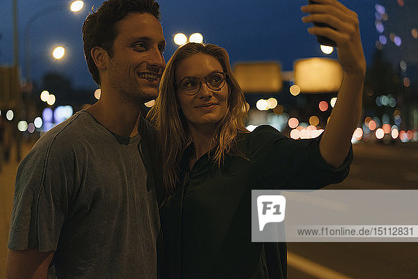 Lächelndes junges Paar beim nächtlichen Selfie in der Stadt