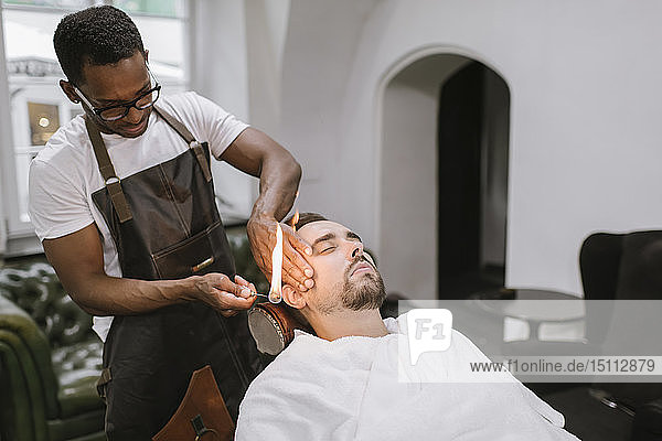Barbier entfernt Ohrhaare eines Kunden mit Feuer im Friseurladen