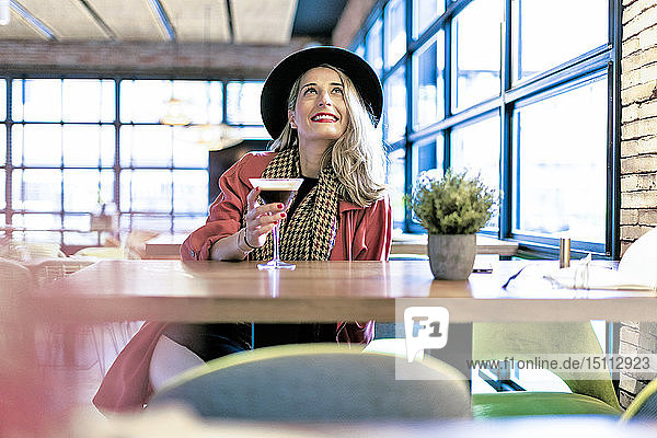 Lächelnde Frau trinkt einen Kaffee-Cocktail in einem Café