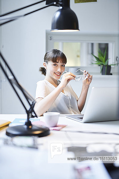 Porträt einer lächelnden jungen Geschäftsfrau  die am Schreibtisch in einem Büro sitzt