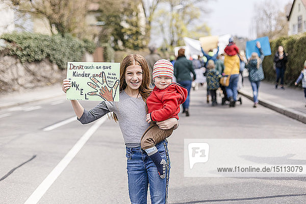 Girl with baby on her arm holding a placard on a demonstration for environmentalism