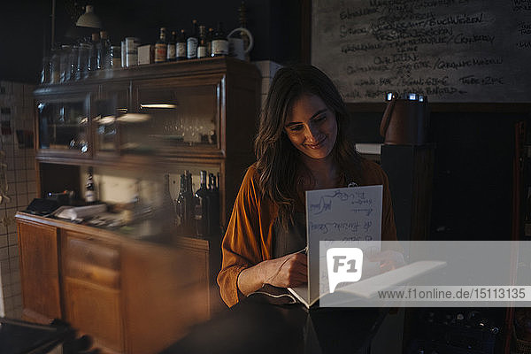 Smiling young woman looking into guestbook at restaurant counter