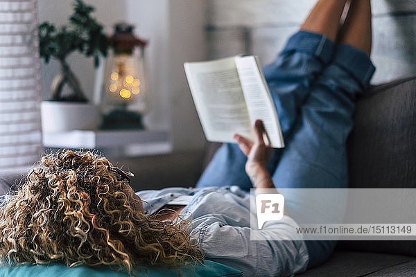 Frau liegt zu Hause auf der Couch und liest ein Buch