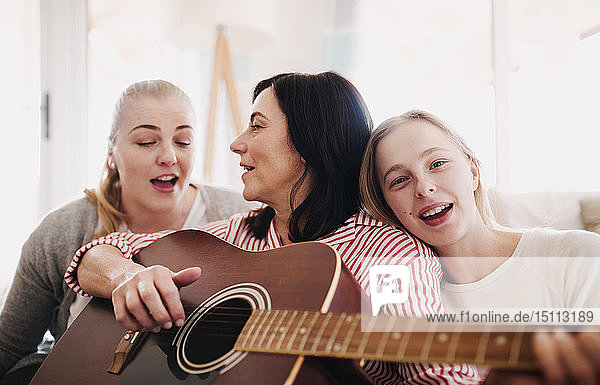 Mature woman with two daughters singing and playing guitar at home