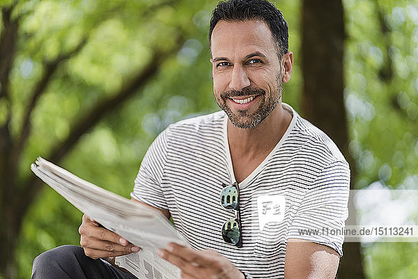 Porträt eines lächelnden Mannes beim Zeitungslesen im Park