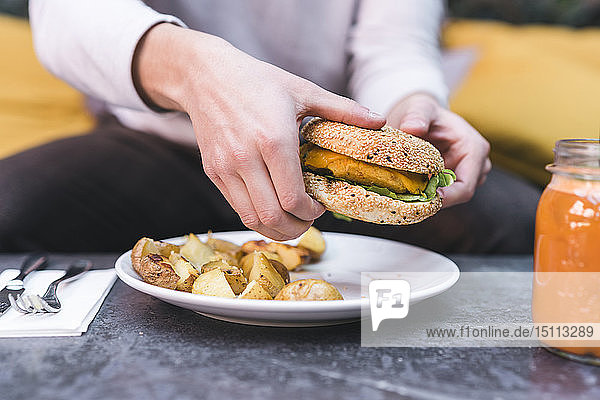 Close-up of man having a vegan burger with potatoes for lunch