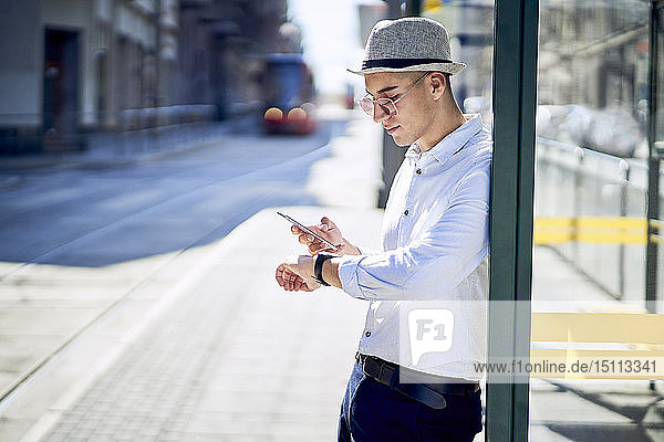 Junger Mann überprüft die Zeit an einer Straßenbahnhaltestelle in der Stadt