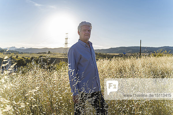 Portrait of senior man standing on a field at sunset