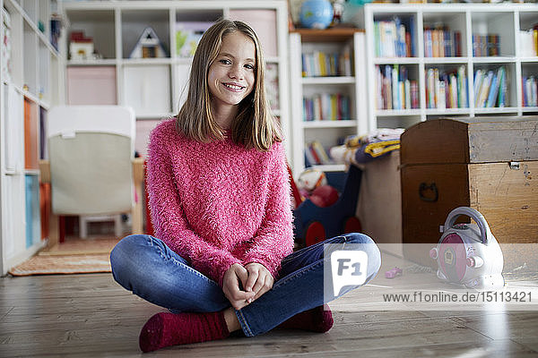 Selbstbewusstes Mädchen sitzt im Schneidersitz auf dem Boden ihres Zimmers