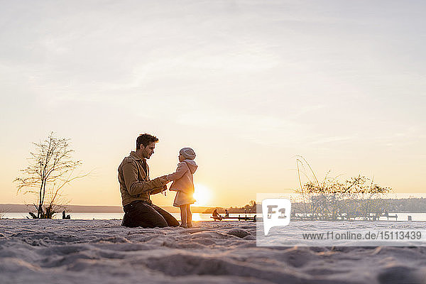 Deutschland Bayern Herrsching Vater und Tochter spielen bei Sonnenuntergang am Strand