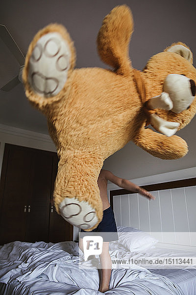 Kleiner Junge steht auf Bett und wirft übergroße Teddybären in die Luft