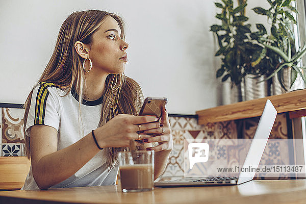 Junge Frau benutzt das Mobiltelefon und den Laptop im Café