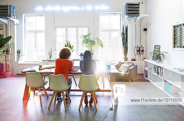 Rückansicht von zwei Frauen  die in einem modernen Büro mit Videoprojektor auf dem Tisch arbeiten