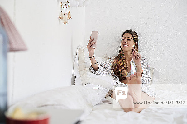 Junge Frau sitzt auf dem Bett und benutzt ein Smartphone