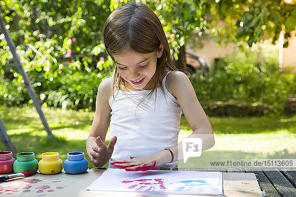 Lächelndes kleines Mädchen  das mit der Hand Farbe auf ein Blatt Papier druckt