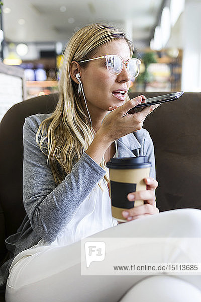 Young woman talking on mobile phone with hands free while drinking a coffee in a coffee shop