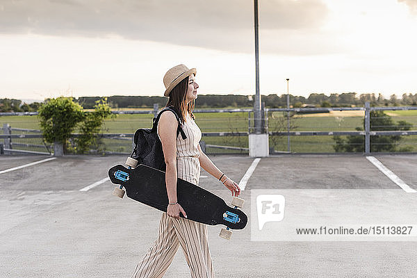 Junge Frau mit Longboard zu Fuss auf dem Parkdeck