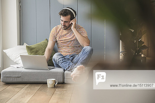 Young man sitting on mattress  using laptop with headphones