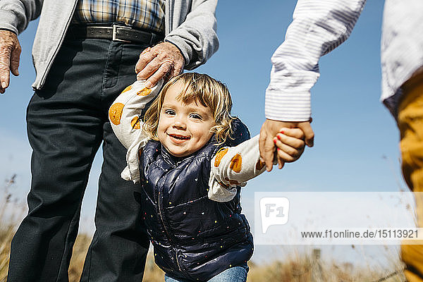 Porträt eines glücklichen kleinen Mädchens  das mit Großvater und Bruder Hand in Hand in der Natur spazieren geht