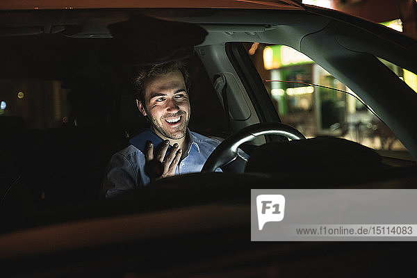Glücklicher junger Mann benutzt nachts sein Handy im Auto