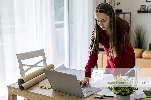 Woman in office working on plan and laptop with wind turbine model on table