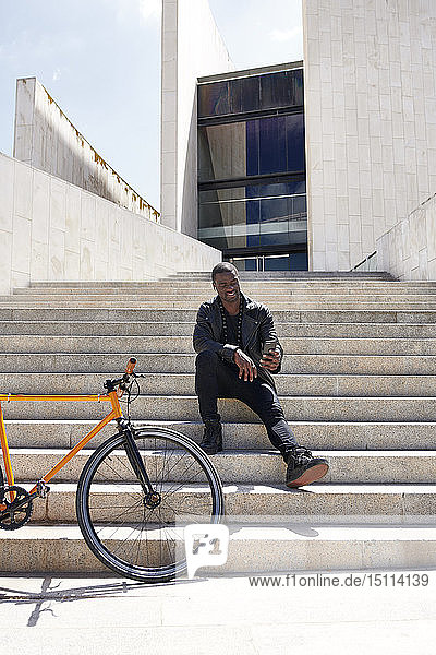 Mann  der ein Selfie macht und auf einer Stufe neben seinem Fahrrad sitzt
