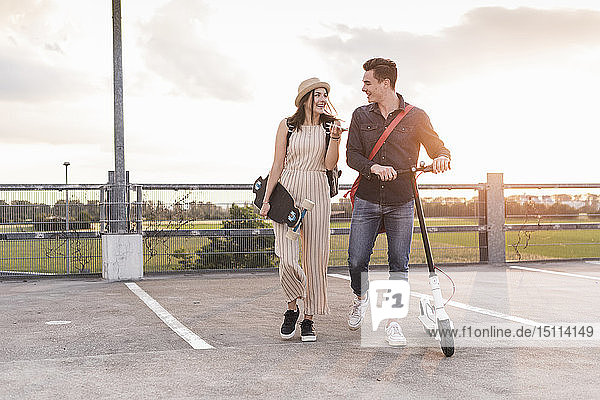 Glückliches junges Paar mit Handy  Longboard und Elektroroller auf dem Parkdeck
