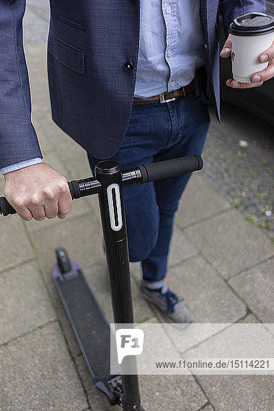 Geschäftsmann mit E-Scooter und Kaffee zum Spazierengehen auf dem Bürgersteig  Teilansicht