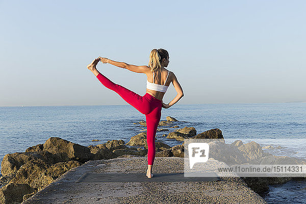 Junge Frau praktiziert Yoga am Strand  macht Stehbalance  Utthita Hasta Padangustasana