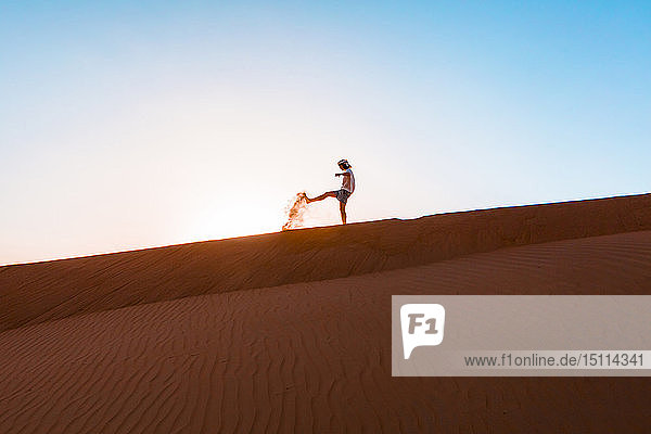 Sultanat Oman  Wahiba Sands  Mittelgroßer Mann spielt mit Sand in der Wüste