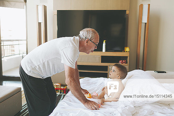 Grossvater spielt zu Hause mit einem Baby mit herausgestreckter Zunge